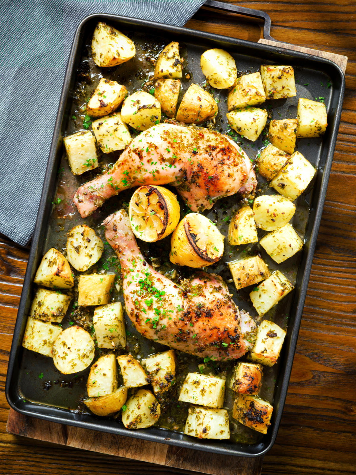 Overhead Greek roasted chicken legs with potatoes, lemon and garlic in a roasting tray.