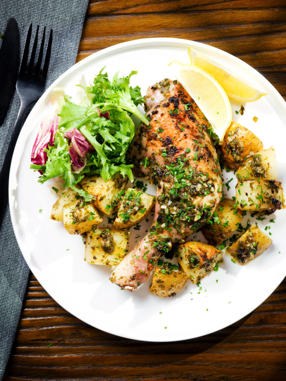 Overhead Greek roasted chicken legs with potatoes, lemon and garlic served with a side salad.