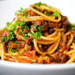 Close up makaronia me kima (Greek spaghetti bolognese) garnished with fresh parsley.