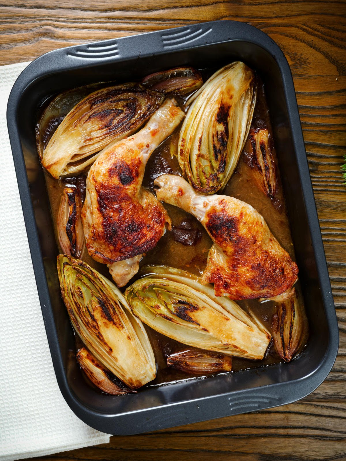 Roasted chicken legs, chicory and shallots in balsamic gravy in a roasting tin.