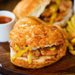Bifana (Portuguese pork sandwich) with mustard on a bun served with French fries.