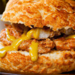 Close-up Bifana (Portuguese pork sandwich) served with mustard on a bun.