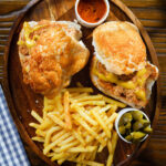 Overhead Bifana (Portuguese pork sandwich) with mustard on a bun, served with French fries and pickles.