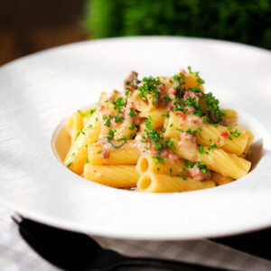 Brie and bacon pasta (rigatoni) in a white bowl garnished with fresh parsley.