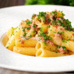 Close-up brie and bacon pasta (rigatoni) garnished with fresh parsley.