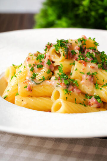 Close-up brie and bacon pasta (rigatoni) garnished with fresh parsley.