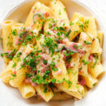 Overhead close-up brie and bacon pasta (rigatoni) garnished with fresh parsley.