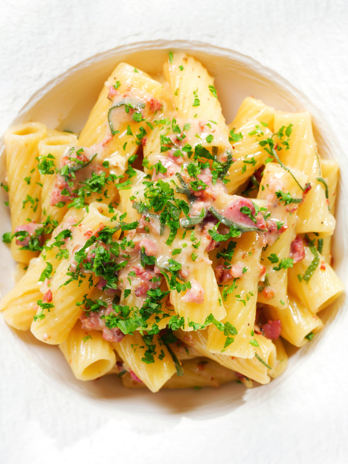 Overhead close-up brie and bacon pasta (rigatoni) garnished with fresh parsley.