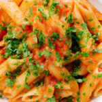 Close-up overhead Bloody Mary Pasta (penne alla vodka), served in a white bowl.