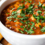 Close-up vegan spicy chickpea and lentil soup garnished with fresh coriander.