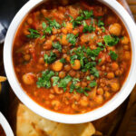 Close-up overhead vegan spicy chickpea and lentil soup garnished with fresh coriander.
