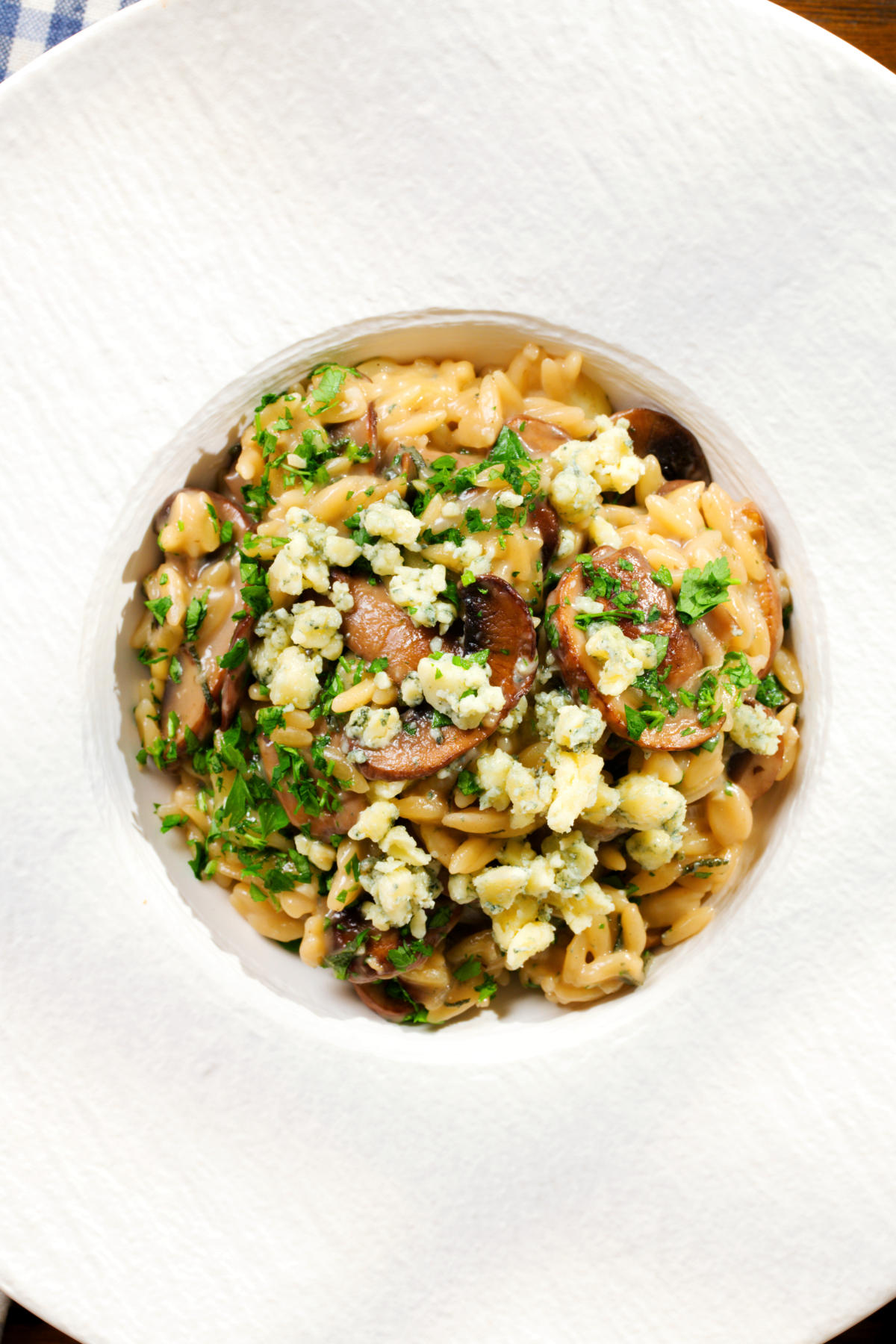 Overhead one-pot stilton cheese and mushroom orzo with sage in a white bowl.