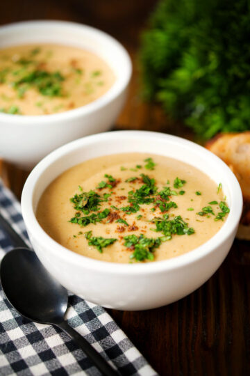 Roasted curried parsnips soup topped with garam masala and coriander served in white bowls.
