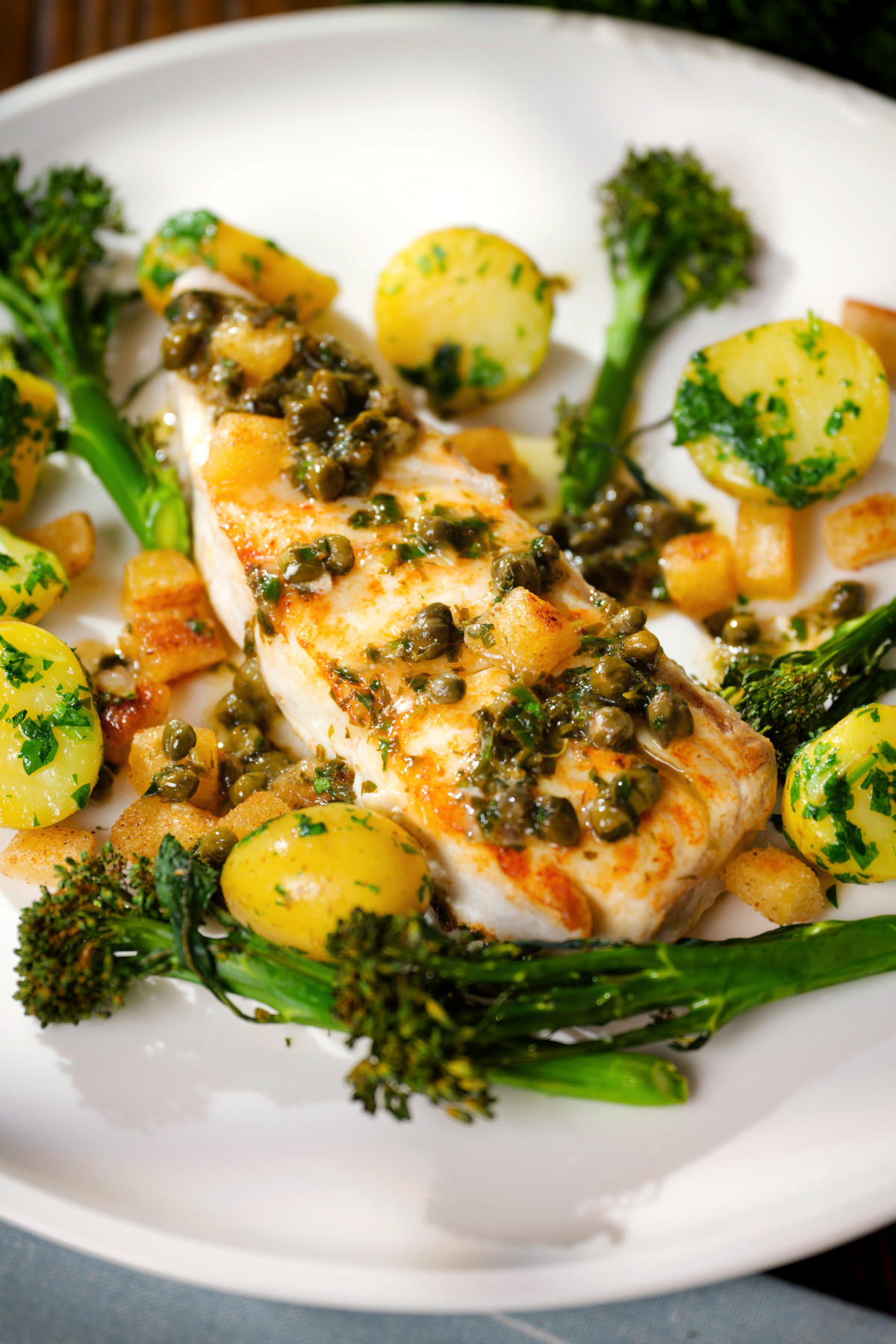 Close-up pan-fried halibut with Grenobloise sauce, buttered potatoes and tenderstem broccoli.