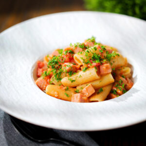 Spam pasta in a tomato and Dijon mustard sauce served in a white bowl.